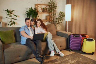 İnternet üzerinden hedef seçiliyor. Mutlu aile, anne, baba ve kız evde oturuyor, dizüstü bilgisayara bakıyor ve yaklaşan seyahati planlıyor. Tatil kavramı, seyahat, rezervasyon hizmetleri