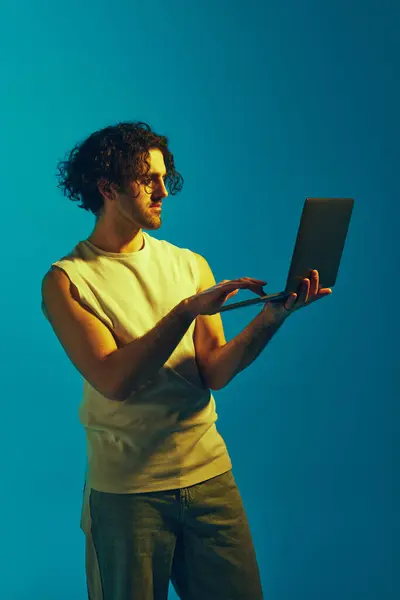 若い男 ネオンライトの青い背景に対してラップトップで作業するカジュアルな服のフリーランサー オンラインサービス 人間の感情 ライフスタイル セールスの概念 — ストック写真