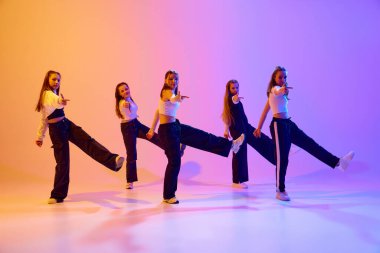 Genç kızların eğitimlerinin dinamik görüntüsü, dans eden hip hop, neon ışıklardaki gradyan stüdyo geçmişine karşı çağdaş dans. Hobi kavramı, gençlik, çocukluk, tarz, moda, dans okulu