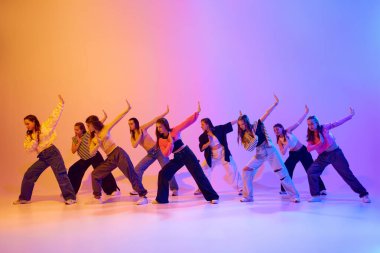 Genç kızların eğitimlerinin dinamik görüntüsü. Dans eden hip hop, modern dans stili, neon ışıkta, gradient stüdyo arka planına karşı. Hobi kavramı, gençlik, çocukluk, tarz, moda, dans okulu