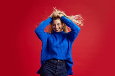 Güzel, zarif, zarif, sarışın bir kadının portresi. Mavi renkte poz veriyor, kırmızı stüdyo arka planına gülümsüyor. İnsan duyguları kavramı, gençlik, moda, ifade