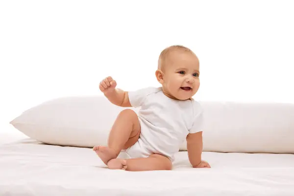 小さな赤ん坊 女の子 白い子供の赤ん坊は枕でベッドに座って微笑み 白い背景に対して厄介な動きをする 幼少期 幼児期 ヒースの概念 — ストック写真