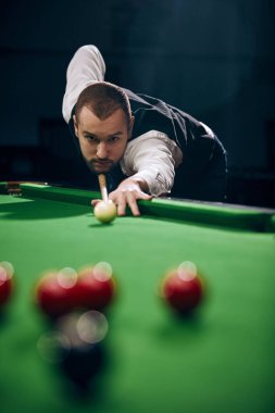 Genç adam kendine güvenerek bilardo masasını inceliyor, bilardo oynuyor. Bilardo dersleri, oyun koçluğu hizmetleri. Bilardo, spor, kumar, hobi, eğlence, oyun kavramı