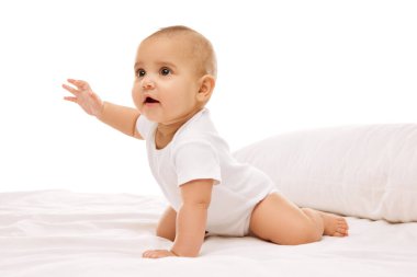 Meraklı, aktif, oyuncu küçük bir kız çocuğu, yastıklarla yatakta oturan, hareketler yapan, beyaz arka plana dikkatlice bakan bir çocuk. Çocukluk kavramı, aile, bakım, annelik, bebeklik, sağlık