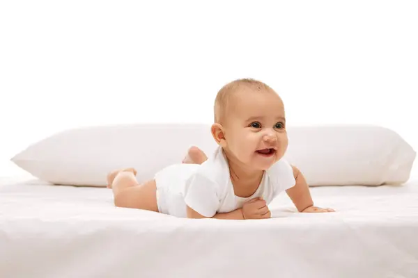 美しい赤ちゃん 白い快適な服の小さな女の子は 白い背景の背後にある枕でベッドの上に横たわっています 幸せとは 幼少期 幼児期 ヒースの概念 — ストック写真