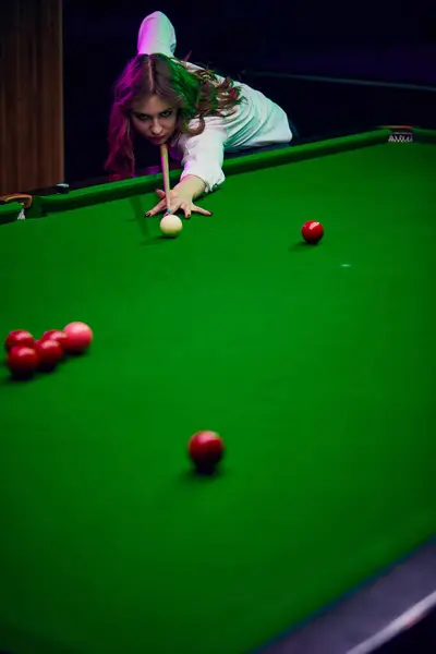 Concentrated young woman leaning on billiards table, playing snooker game. Lifestyle magazine about leisure activities. Concept of billiards sport, gambling, hobby, leisure, game