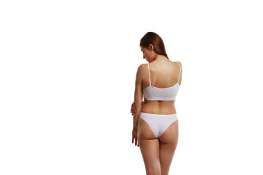 Sağlıklı, zayıf, formda, iç çamaşırlarıyla beyaz stüdyo arka planında duran güzel bir kızın arka plan görüntüsü. Vücut ve sağlık, spor, kadın güzelliği, sağlık kavramı
