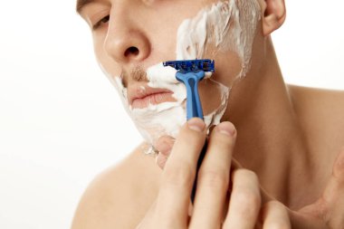 Odaklanmış, üstsüz, beyaz stüdyo geçmişiyle traş olan genç bir adama yakın plan. Kesilmiş fotoğraf. Güzellik ve güven. Güzellik tedavisi, erkek sağlığı, vücut bakımı, kaplıca tedavisi, hijyen.