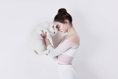 Hayvana bağlı, evcil hayvan arkadaşlarıyla bağ kuruyor. Beyaz elbiseli genç bir kız beyaz kediyi beyaz stüdyo arka planında tutuyor. Aşk kavramı, hayvan bakımı, sağlık.