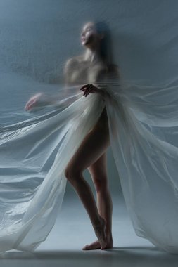 Gri arka planda şeffaf, mat, dokulu materyalle çıplak poz veren genç bir kadının tam boy silueti. Vücut estetiği kavramı, kadınlık, güzellik, sağlık, sanat