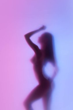 Sıska, formda, neon rengi arka planda çıplak poz veren zarif bir kadının bulanık silüeti. Özgürlük ve kendini sevme. Vücut estetiği kavramı, kadınlık, güzellik, sağlık, sanat