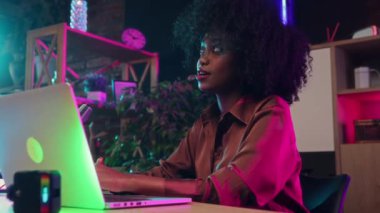 Afrikalı genç bir kadın, gazeteci, kendi podcast 'ini kaydediyor, mikrofon ve dizüstü bilgisayar kullanıyor, merkez ofiste görüşmeler yapıyor. Çevrimiçi iletişim kavramı, modern teknoloji, kitle iletişim
