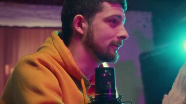 Genç adam merkez ofiste mikrofon ve dizüstü bilgisayarla oturuyor, online podcast kaydediyor, konuşuyor. Sosyal medya işi. Çevrimiçi iletişim kavramı, modern teknoloji, kitle iletişim