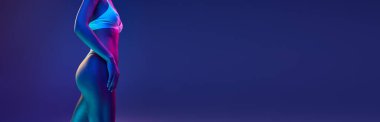 İnce ve mükemmel bir kadın modeli. İç çamaşırlarıyla, çok renkli neon ışıklarıyla gradyan mavi stüdyo arka planına poz veriyor. Uzayı kopyala Güzellik kavramı, spa prosedürleri, cilt bakımı, kozmetoloji.