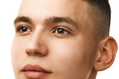 Beyaz stüdyo arka planında, pürüzsüz, tıraşlı, kahverengi gözlü ve kısa saçlı yakışıklı bir gencin yakın plan portresi. Erkek güzelliği, deri ve vücut bakımı, hijyen, erkek kozmetiği kavramı