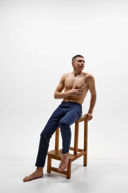 Kaslı, üstsüz, omuzunda doğum lekesi olan, kot pantolonlu, beyaz stüdyo arka planında izole bir şekilde poz veren yakışıklı bir genç. Spor yaşam tarzı kavramı, vücut ve sağlık hizmetleri, gençlik