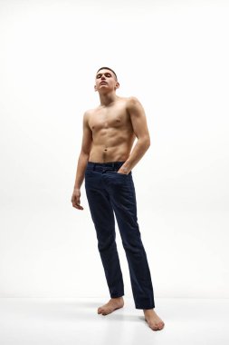 Beyaz stüdyo arka planında izole edilmiş kot pantolonla poz veren yakışıklı, kendine güvenen, üstsüz bir adamın tam boy görüntüsü. Spor yaşam tarzı kavramı, vücut ve sağlık hizmetleri, gençlik