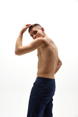 Gömleksiz yakışıklı, kaslı vücutlu, omuzunda doğum lekesi olan beyaz stüdyo arka planında izole edilmiş kot pantolonla dolaşan genç bir adam. Spor yaşam tarzı kavramı, vücut ve sağlık hizmetleri, gençlik