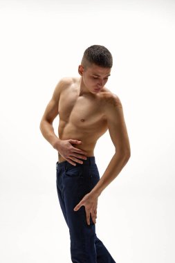 Gömleksiz yakışıklı, kaslı, rahatlamış, beyaz stüdyo arka planında izole edilmiş kot pantolonla poz veren genç bir adam. Spor yaşam tarzı kavramı, vücut ve sağlık hizmetleri, gençlik