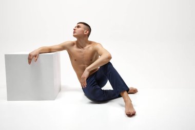 Beyaz stüdyo arka planında izole edilmiş kot pantolonla poz veren sağlıklı, rahatlatıcı, kaslı genç bir adam. Spor yaşam tarzı kavramı, vücut ve sağlık hizmetleri, gençlik