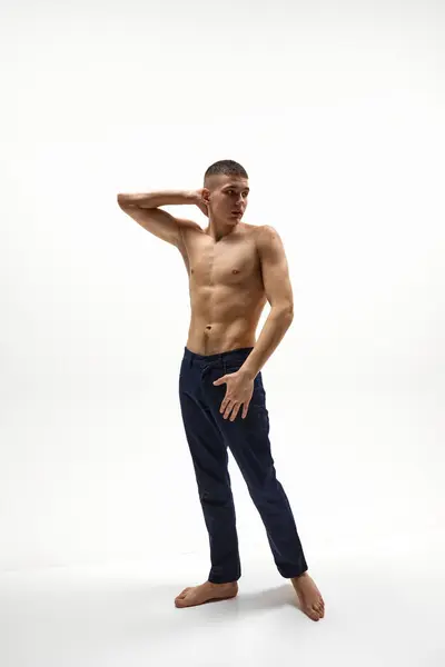 Full-length image of handsome young shirtless guy with muscular, relief body shape posing in jeans isolated over white studio background. Concept of sportive lifestyle, body and heath care, youth