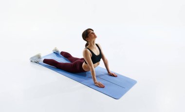 Vücut durumundan sonra bakımını üstlenen sıska bir kadın, yoga egzersizleri yapıyor, beyaz arka planda izole bir şekilde kobra pozu veriyor. Spor, sağlık ve vücut bakımı, fitness uygulaması, egzersiz şablonları