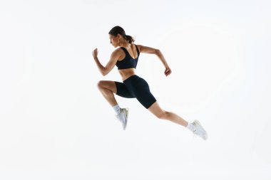 Genç bir kadının dinamik görüntüsü. Güçlü, sağlıklı spor kıyafetleri içinde hareket halinde. Eğitimi beyaz stüdyo arka planında izole edilmiş. Spor, sağlık ve vücut bakımı kavramı, fitness uygulaması