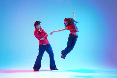 Güzel genç bir kadın dinamik bir poz içinde dans ederken bir adam mavi arka plana hayranlıkla bakarken neon ışıkta. Retro dans. Hobi kavramı, dans sınıfı, parti, 50 'ler, 60' lar kültürü, gençlik