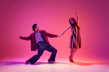 Sanatçı genç bir adam ve zarif bir kadın şık kostümler içinde dans eden çift neon ışıkta pembe arka plana karşı. Hobi kavramı, dans sınıfı, parti, 50 'ler, 60' lar kültürü, gençlik