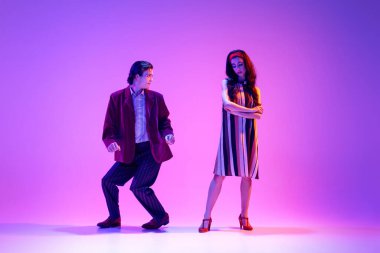 Artistik, yetenekli, pozitif erkek ve kadın, şık bir çift dans ediyor, neonlu mor arka planda boogie woogie yapıyor. Hobi kavramı, dans sınıfı, parti, 50 'ler, 60' lar kültürü, gençlik