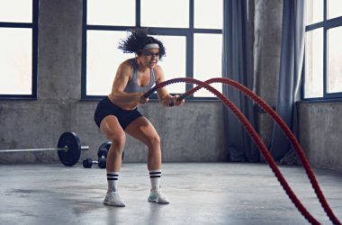 Spor kıyafetli genç bir kadının dinamik portresi fitness merkezinde halat çalışması yapıyor. Başla. Profesyonel spor, vücut geliştirme, aktif ve sağlıklı yaşam tarzı, enerji.