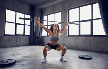 Spor giyimli genç bir kızın spor salonundaki halterle spor yaparken dinamik portresi. Güç ve güç. Profesyonel spor anlayışı, aktif yaşam tarzı, vücut geliştirme. Ad