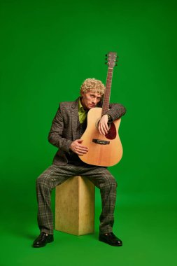Tutkulu bir müzisyen. Takım elbiseli kıvırcık genç adam yeşil stüdyo arka planında gitar çalıyor. Canlı müzik etkinliği. Müzik, performans, sanat, eğlence, festival, performans, reklam kavramı