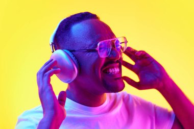 Afro-Amerikalı bir adamın portresi duygusal olarak kulaklıkla müzik dinliyor ve sarı stüdyo ışıklarıyla şarkı söylüyor. İnsan duyguları kavramı, gündelik moda, yaşam tarzı