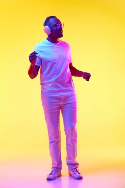 Gündelik giysiler içinde, kulaklıkla müzik dinleyen ve sarı stüdyo ışıklarıyla dans eden Afro-Amerikan bir adam. İnsan duyguları kavramı, gündelik moda, yaşam tarzı