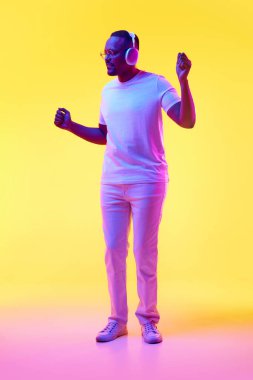 Gündelik giysiler içinde, kulaklıkla müzik dinleyen ve sarı stüdyo ışıklarıyla dans eden Afro-Amerikan bir adam. İnsan duyguları kavramı, gündelik moda, yaşam tarzı