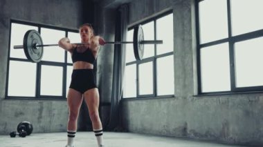 Modern spor salonunda ağırlık kaldırırken çömelme hareketleri yapan güçlü genç bir kadın. Profesyonel spor anlayışı, aktif yaşam tarzı, vücut geliştirme, enerji, aksiyon. Reklam. Video, 4k