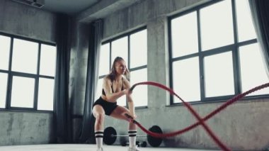 Odaklanmış genç atlet kadın şehir fitness sahasında savaş halatları kullanarak çalışıyor. Motivasyon. Profesyonel spor, vücut geliştirme, aktif ve sağlıklı yaşam tarzı, güç. Ad