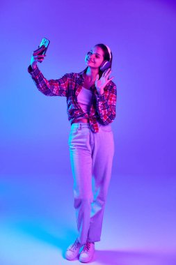 Damalı tişörtlü, cep telefonuyla konuşan gülümseyen genç bir kadının tam boy görüntüsü neon renkli mor stüdyo arka planıyla karşılaşıyor. Gençlik kavramı, yaşam tarzı, gündelik moda, insani duygular
