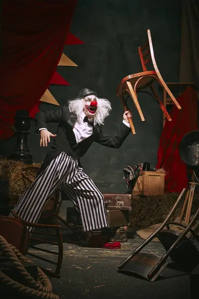 黒い帽子 赤い鼻とストライプのズボンが付いている白い顔で 暗いレトロサーカスの背部の背景の椅子と性能を作ります サーカス パフォーマンス ショー レトロ ヴィンテージのコンセプト — ストック写真