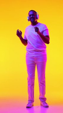Gündelik giysiler içinde, kulaklıkla müzik dinleyen ve sarı stüdyo ışıklarıyla dans eden Afro-Amerikan bir adam. İnsan duyguları kavramı, gündelik moda, yaşam tarzı