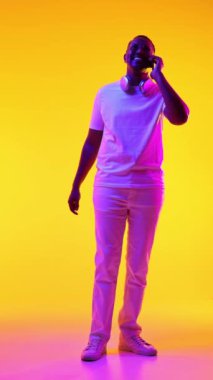 Normal kıyafetlerle gezen, cep telefonuyla konuşan ve sarı ışıkta dans eden Afro-Amerikan bir adam. İnsan duyguları kavramı, gündelik moda, yaşam tarzı