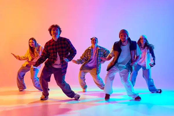 Talented young people, friends in motion, dancing hip hop, training against gradient studio background in neon light. Concept of modern dance style, hobby, active lifestyle, youth culture