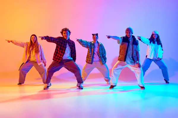 Artistic five dancers, young man and woman in motion, dancing against gradient studio background in neon light. Concept of modern dance style, hobby, active lifestyle, youth culture
