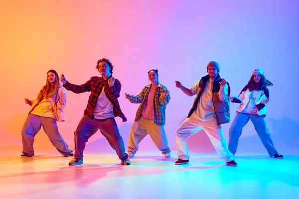 stock image Group of five dancers in casual clothes performing with synchronized poses against gradient studio background in neon light. Concept of modern dance style, hobby, active lifestyle, youth culture