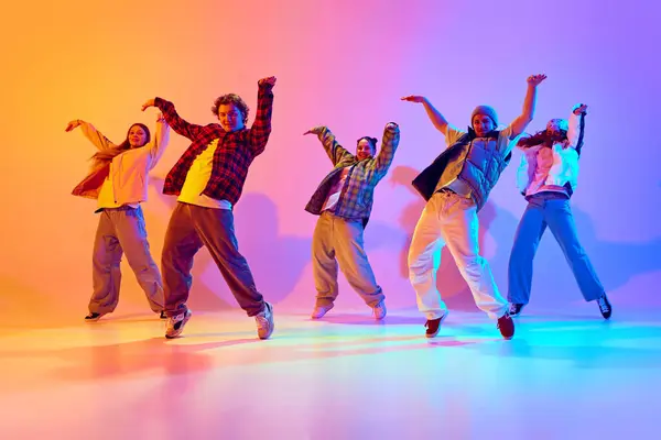 Synchronized movements. Group of young people dancing contemp against gradient studio background in neon light. Concept of modern dance style, hobby, active lifestyle, youth culture