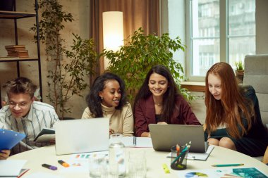 Motive olmuş gençler, masada dizüstü bilgisayarlarla oturan öğrenciler, üniversite görevleri yapan, birlikte proje hazırlayan öğrenciler. Eğitim, gençlik, bilgi, ödev, sınavlar, projeler kavramı.