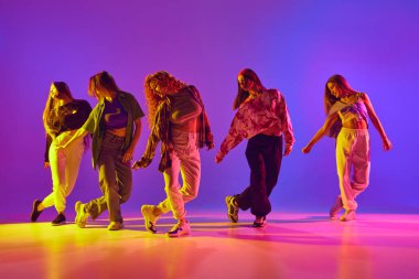 Hareket halindeki sanatsal genç kadınlar, gündelik kıyafetler giyip dans ediyorlar, neon ışıkta serbest stil dansı yapıyorlar. Gençlik kavramı, sokak dansı, modern dans, modern dinamik.