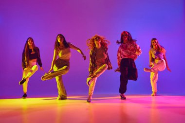 Hareket halindeki sanatsal genç kadınlar, gündelik kıyafetler giyip dans ediyorlar, neon ışıkta serbest stil dansı yapıyorlar. Gençlik kavramı, sokak dansı, modern dans, modern dinamik.