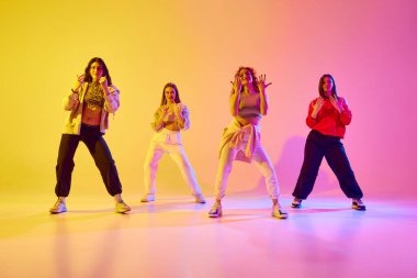 Spor tarzı gündelik giysiler içinde dört sanatsal genç kadın neonlu arka planda serbest dans ediyorlar. Gençlik kavramı, sokak dansı, modern dans, modern dinamik.